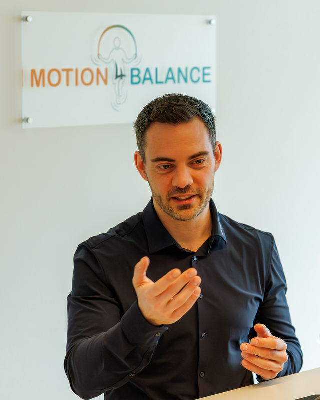 Markus Stilp im Coaching-Gespräch vor dem Motion4Balance Logo in seinem Studio in Regensburg